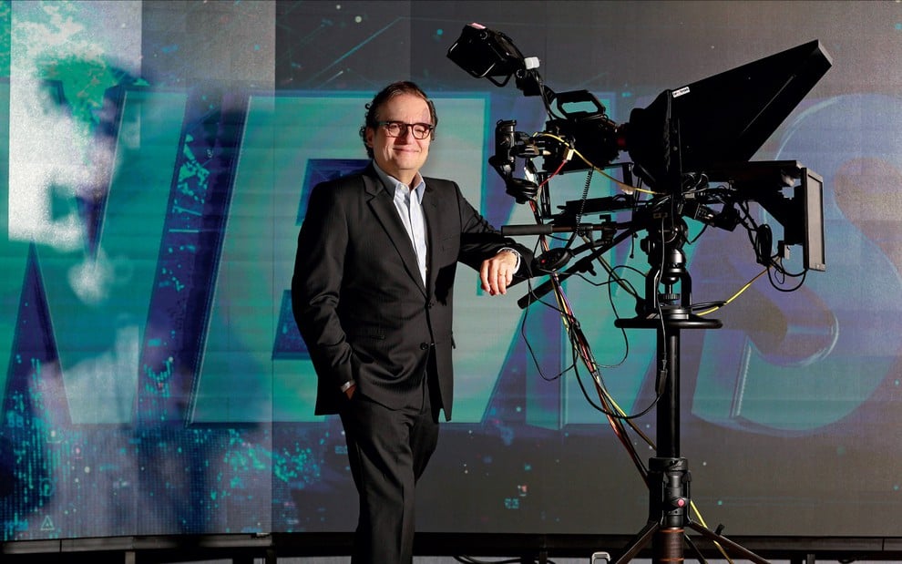 Antônio Augusto Amaral de Carvalho Filho, o Tutinha, usa um terno preto com blusa azul e se apoia em uma câmera dos estúdios de televisão da Jovem Pan