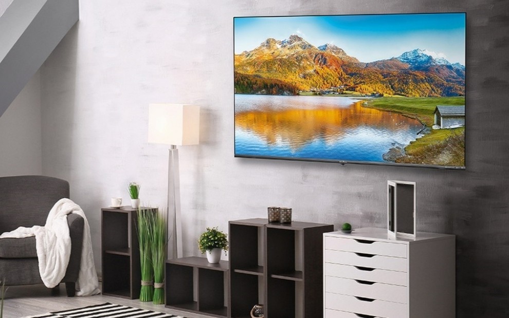 TV, pendurada em uma parede de uma sala, mostra uma paisagem de montanha e rio