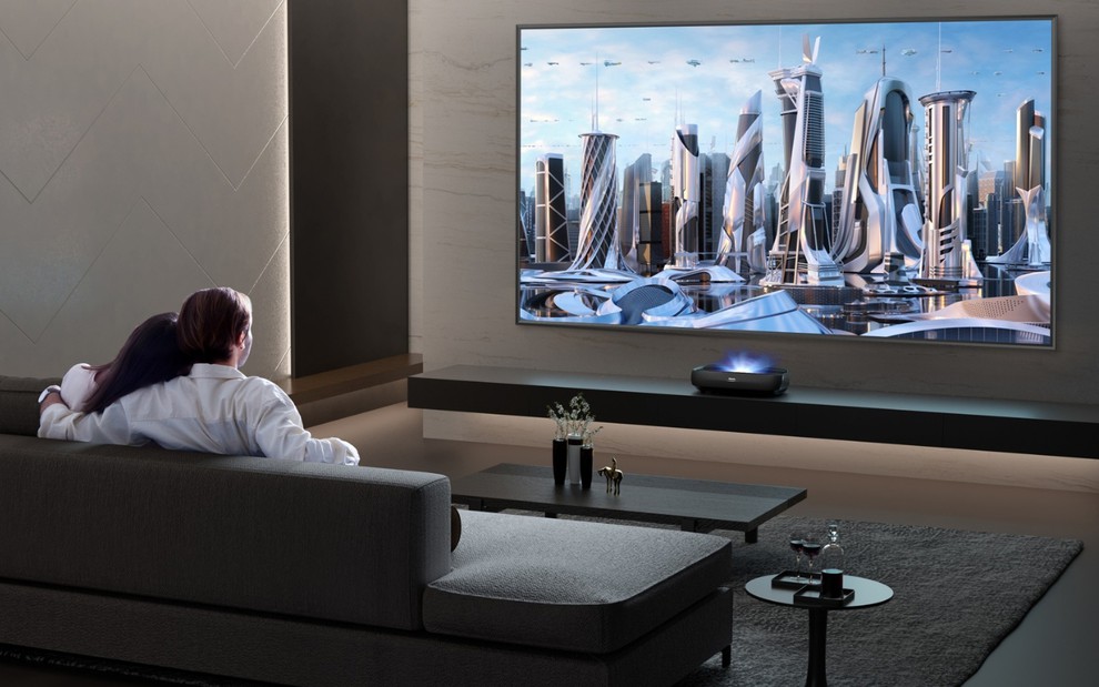 Casal acompanha imagens da TV a laser em sala decorada