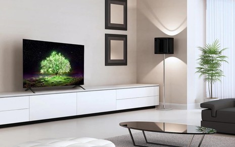 Uma sala com decoração clara em que há uma TV no rack, dois quadros na parede, uma mesa de centro e um abajur perto da janela