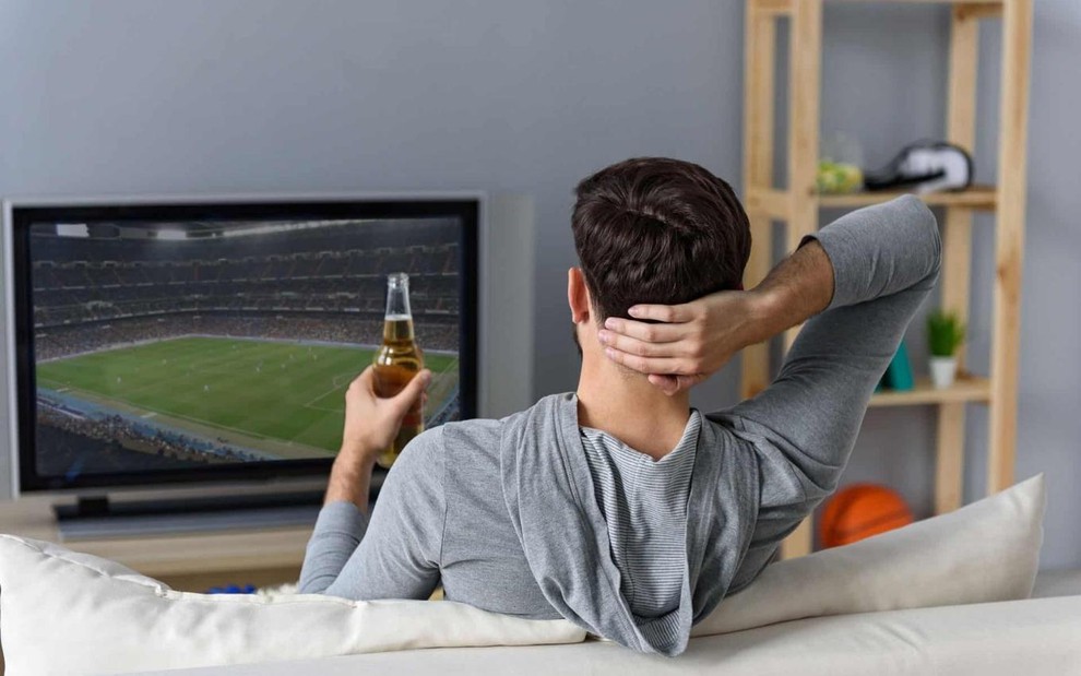 Telespectador vendo jogo de futebol na TV de tela fina da sala