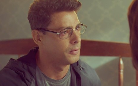 O ator Cauã Reymond de perfil, de óculos, com expressão séria, em cena como Christian em Um Lugar ao Sol