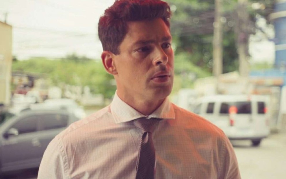 O ator Cauã Reymond de camisa branca, gravata, olha para a direita com expressão séria em cena de Um Lugar ao Sol