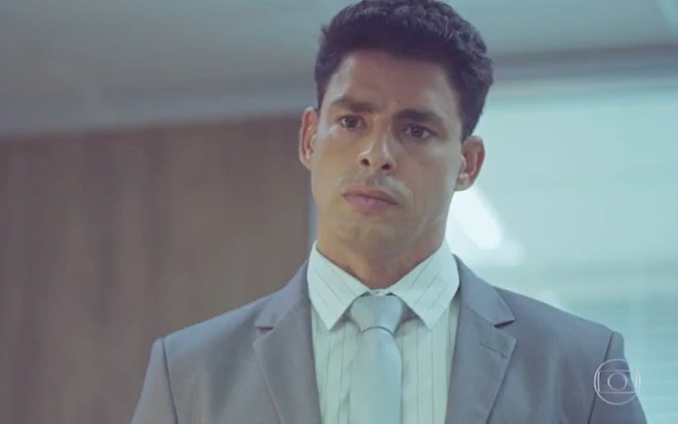 O ator Cauã Reymond com expressão séria, de terno cinza, em cena como Christian em Um Lugar ao Sol