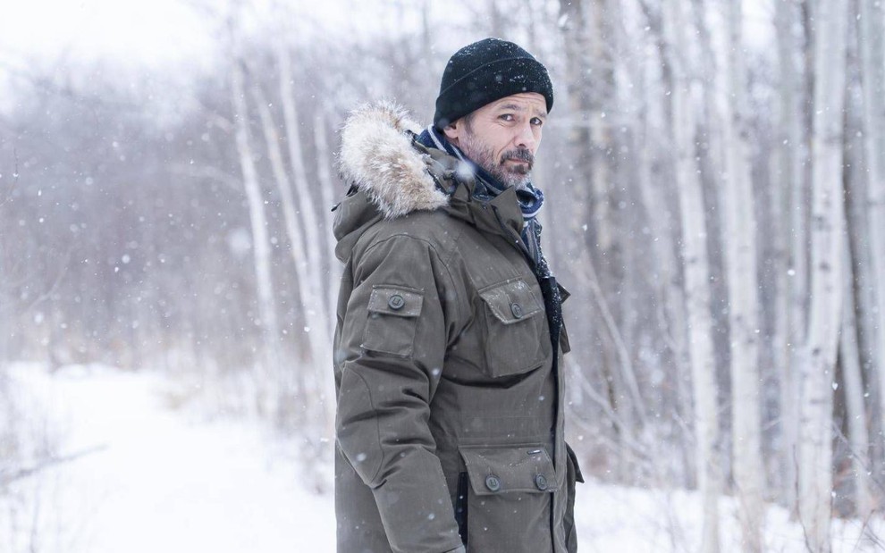 Billy Campbell veste casaco de frio e touca em meio a uma floresta congelada