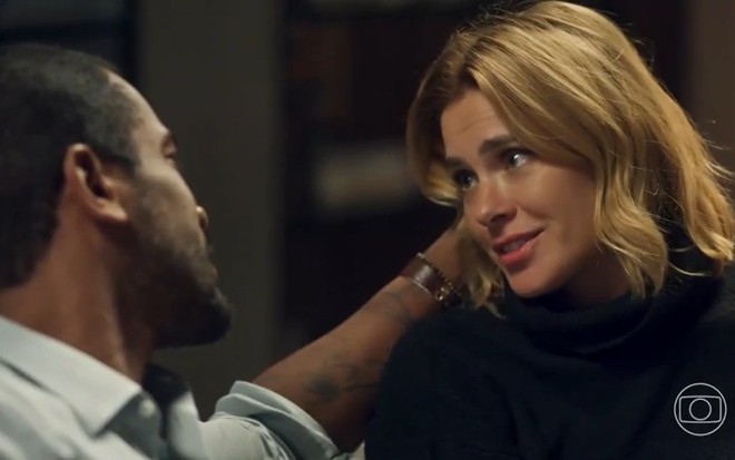 Os atores Samuel de Assis e Carolina Dieckmann frente a frente, conversando em sala de apartamento, em cena de Vai na Fé