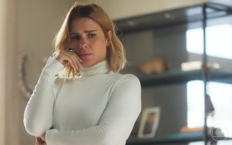 Em cena de Vai na Fé, Carolina Dieckmann usa uma blusa branca de gola alta e parece estar tensa