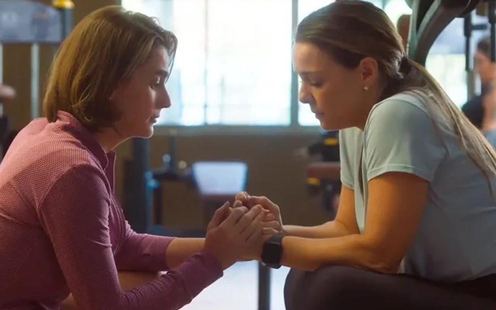 Em cena de Vai na Fé, Priscila Sztejnman segura a mão de Regiane Alves como se estivesse consolando a amiga