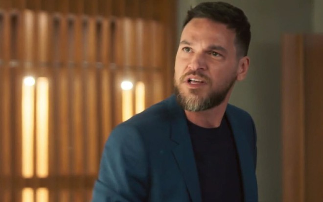 Emilio Dantas com expressão séria em cena como Theo na novela Vai na Fé
