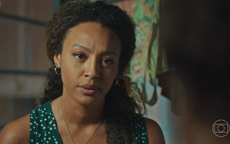 Em cena de Vai na Fé, Sheron Menezzes usa blusa verde com estampa de flores pequenas; ela está falando com alguém