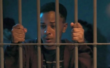 O ator Jean Paulo Campos atrás de grades numa cadeia, com expressão de desespero em cena de Vai na Fé