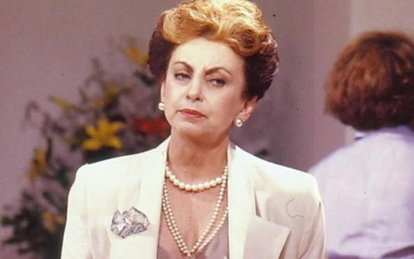A atriz Beatriz Segall com expressão séria terninho branco e colar de pérolas em cena como Odete Roitman em Vale Tudo