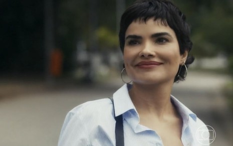Em cena de Travessia, Vanessa Giácomo está usando uma blusa social branca, brinco de argolas prateado e está sorrindo