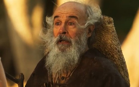 Osmar Prado usa barba longa e um manto e está caracterizado como o Velho do Rio para a novela Pantanal