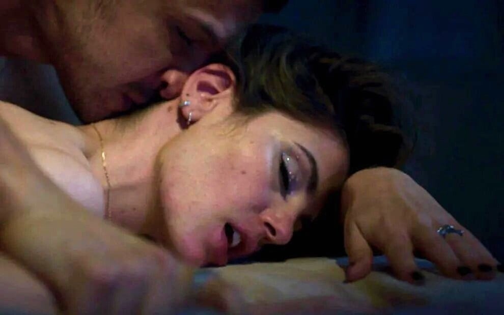 A atriz Camila Queiroz está deitada numa cama, com os olhos fechados, enquanto Romulo Estrela beija seu pescoço em gravação de Verdades Secretas 2