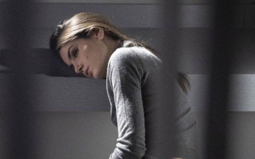 Angel (Camila Queiroz) está sentada no chão de cela de cadeia em cena de Verdades Secretas 2