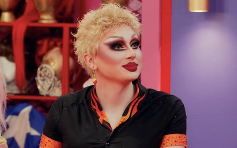 A drag queen Maddy Morphosis com uma peruca curta, loira, e maquiagem pesada com um figurino inspirado no cozinheiro Guy Fieri no Werk Room de Drag Race