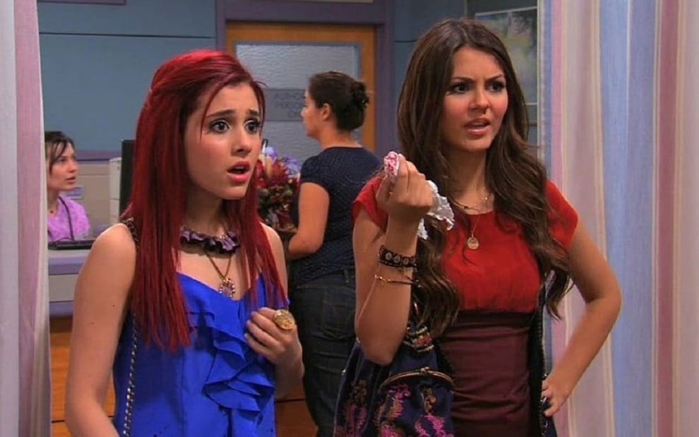 Ariana Grande como Cat e usa uma blusa azul, enquanto Victória Justice usa um vestido vermelho