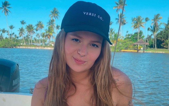 Viih Tube posando em um barco na praia em seu Instagram. Ela está sorrindo de boca fechada e usa um boné preto e um biquíni rosa