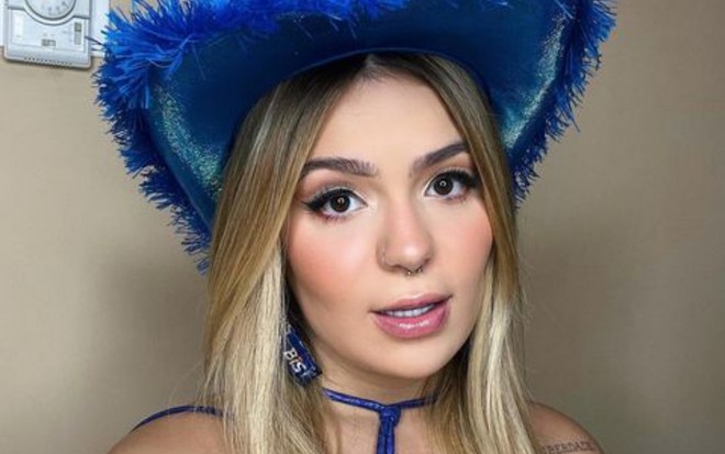 Viih Tube de chapéu azul de plumas e maquiagem marcada