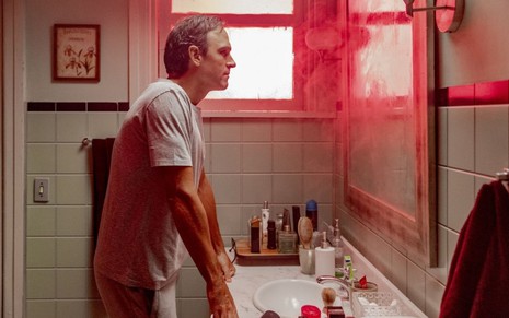De frente para o espelho de um banheiro, Tadeu Schmidt veste pijamas cinzas