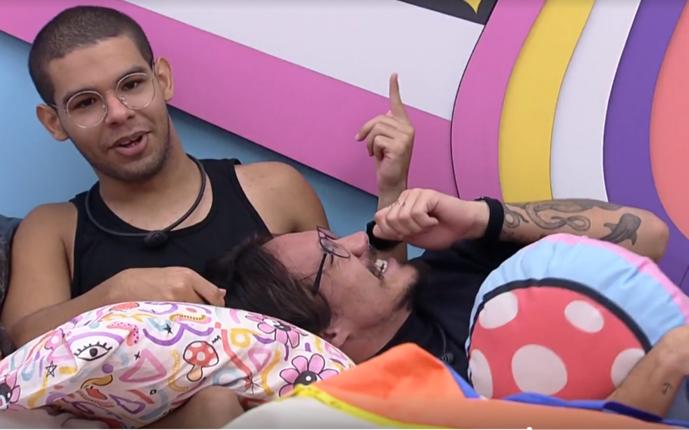 No quarto lollipop, Vinicius Fernandes está sentado sobre uma cama e seu colega Eliezer Netto está com a cabeça apoiada sobre um travesseiro no colo do amigo