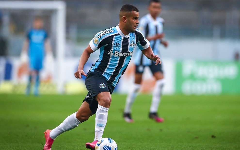 Alisson correndo em jogo do Grêmio na Arena do Grêmio; ele está com o uniforme tradicional do clube