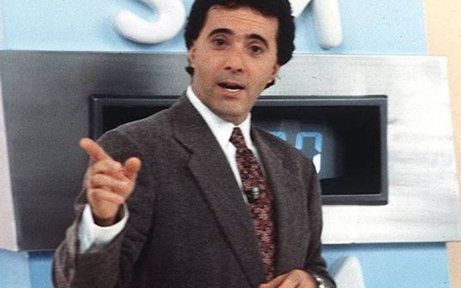 Tony Ramos na apresentação do Você Decide (1992-2000), de terno, camisa e gravata, dedo indicador direito apontado para a direita