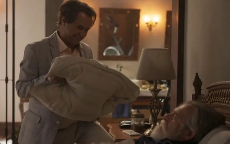 Sabá Bodó (Welder Rodrigues) segura um travesseiro na direção do rosto de Tertúlio (José de Abreu), que está dormindo