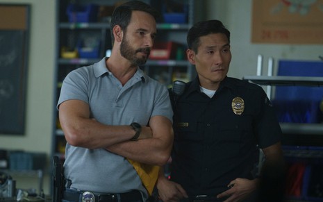 Os atores Rodrigo Santoro e Lanny Joon em cena de Wolf Pack, lado a lado, com uniformes de policiais
