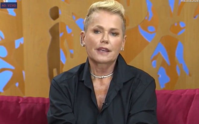 Xuxa no cenário do programa Saia Justa. Ela usa uma camisa preta e tem a expressão séria