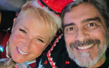 Xuxa Meneghel e Junno Andrade em foto publicada no Instagram, ambos estão abraçados e sorrindo, ela veste um chapéu natalino e ele veste um suéter com estampa natalina