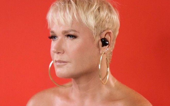 Xuxa Meneghel em close, olha para a esquerda em ensaio de fotos com fundo vermelho