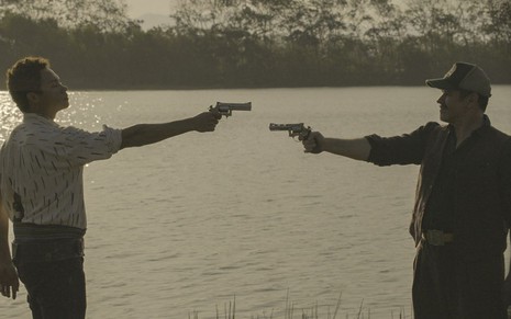 Em cena de Pantanal, Silvero Pereira e Silvero Pereira estão com duas armas apontadas um para o outro