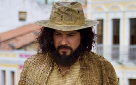 Sergio Guizé com cabelo e barba grandes e usando um chapéu de palha em cena como Zé Paulino na novela Mar do Sertão