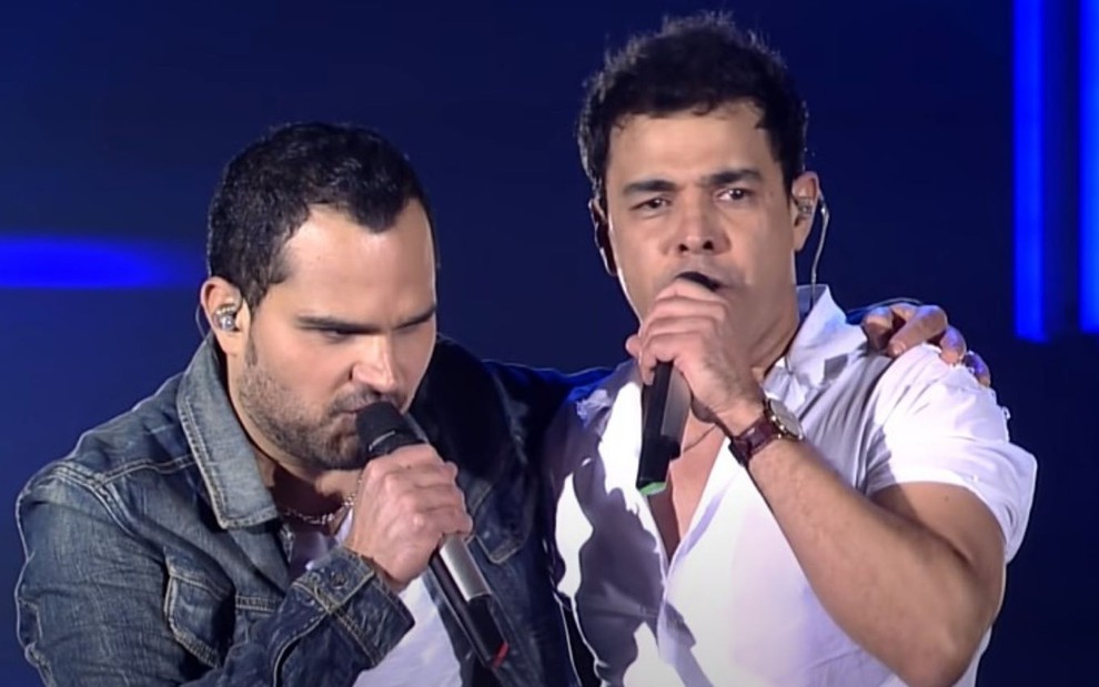 Luciano e Zezé Di Camargo abraçados enquanto cantam em show disponível para assistir no YouTube