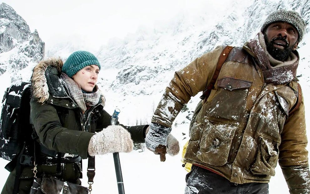 Kate Winslet e Idris Elba estão no meio da neve em cena do filme Depois Daquela Montanha