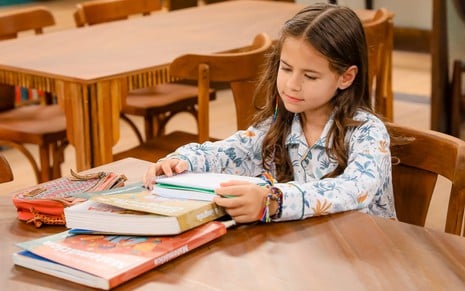 Mel Summers está de pijama, sentada à mesa com livros didáticos