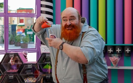 Phil Miler usa uma camisa social azul e tem a barba ruiva; ele segura um medidor e derruba discos de chocolate numa vasilha