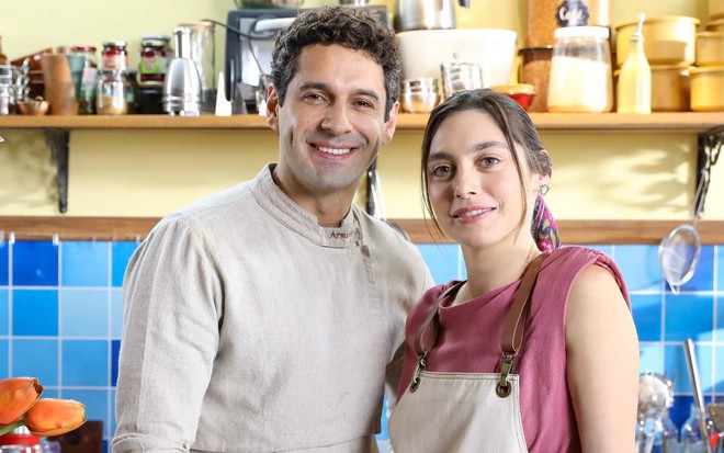 Os atores João Baldasserini e Juliana Schalch lado a lado, sorrindo, em cenário de A Infância de Romeu e Julieta