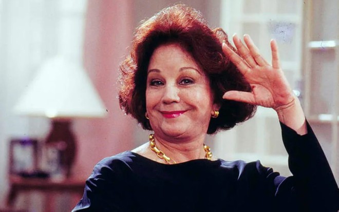 A atriz Lolita Rodrigues (1929-2023) na novela A Viagem (1994), sorrindo de boca fechada, com mão próxima à cabeça