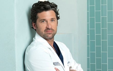 Patrick Dempsey posa com jaleco branco e encostado em parede do hospital de Grey's Anatomy