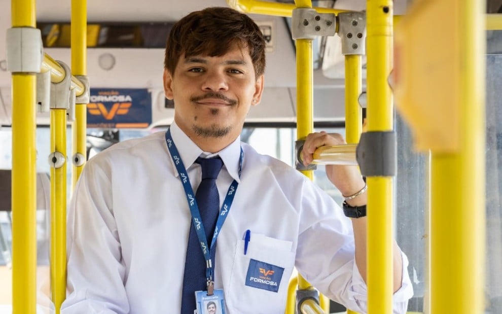 Adanilo Reis caracterizado como Sidney; ele usa uma roupa social e um crachá da Viação Formosa. O ator posa dentro de um ônibus em ensaio de divulgação de Volta por Cima