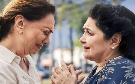 Em cena de Terra e Paixão, Eliane Giardini está chorando apertando a mão de Inez Viana