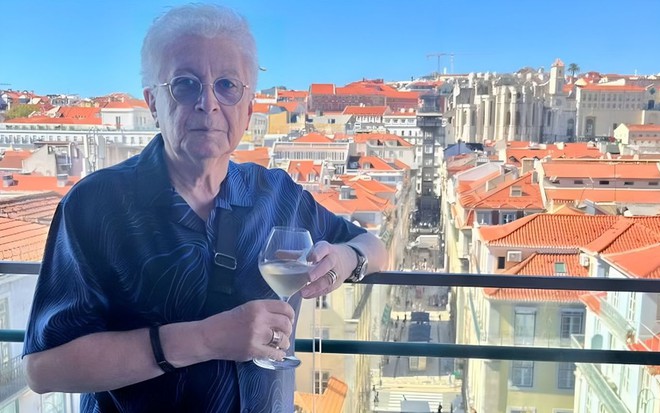 Aguinaldo Silva está com uma taça de vinho em um terraço de Lisboa