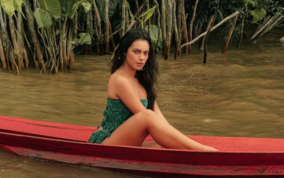 Alane Dias usa maiô verde e está em uma jangada vermelha em um rio