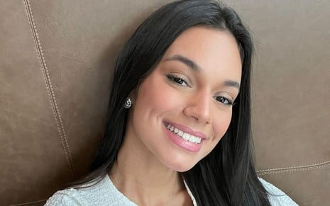 Alane Dias posa sorrindo usando uma blusa branca