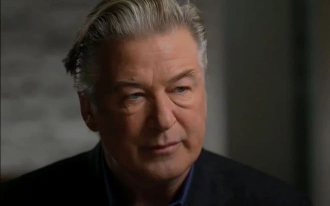 Alec Baldwin usa um terno preto e está sério em entrevista ao ABC