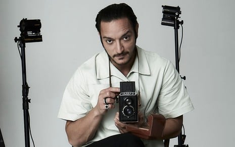 Allan Souza Lima segura uma câmera antiga na mão e olha para frente