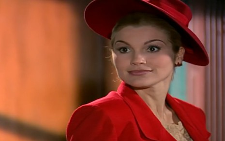 A atriz Flávia Alessandra com expressão séria, chapéu e terno vermelhos em cena de Alma Gêmea
